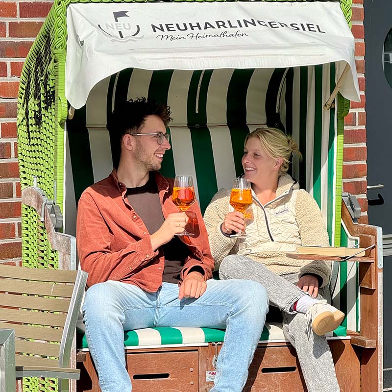 Junges Paar stößt im grün-weißen Strandkorb an
